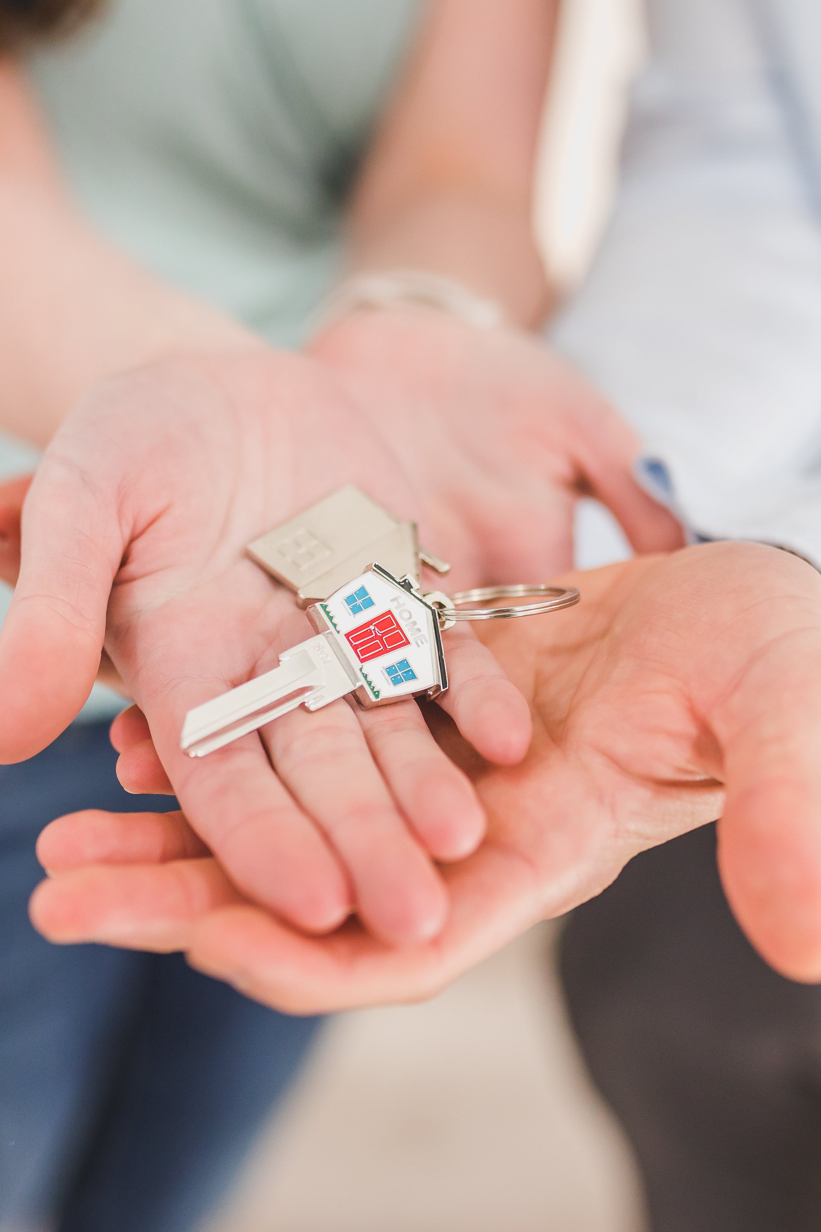 Two hands holding a set of keys with a house-shaped keychain, symbolizing home ownership or real estate purchase.